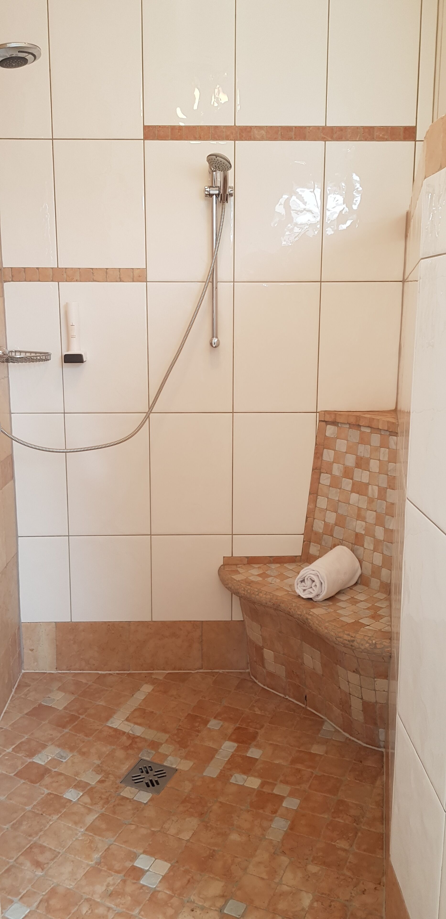 Un bagno con doccia, un asciugamano su un ripiano e un pavimento piastrellato.