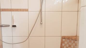 Un bagno con doccia, un asciugamano su un ripiano e un pavimento piastrellato.