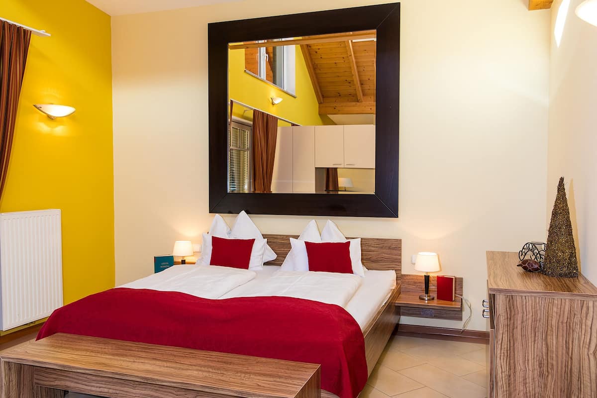 A hotel room with a bed, bedside tables, a mirror, and a red and white color scheme.