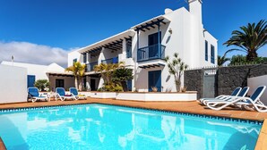 Une villa moderne dotée d’une piscine, de chaises longues et d’un mur en pierre.
