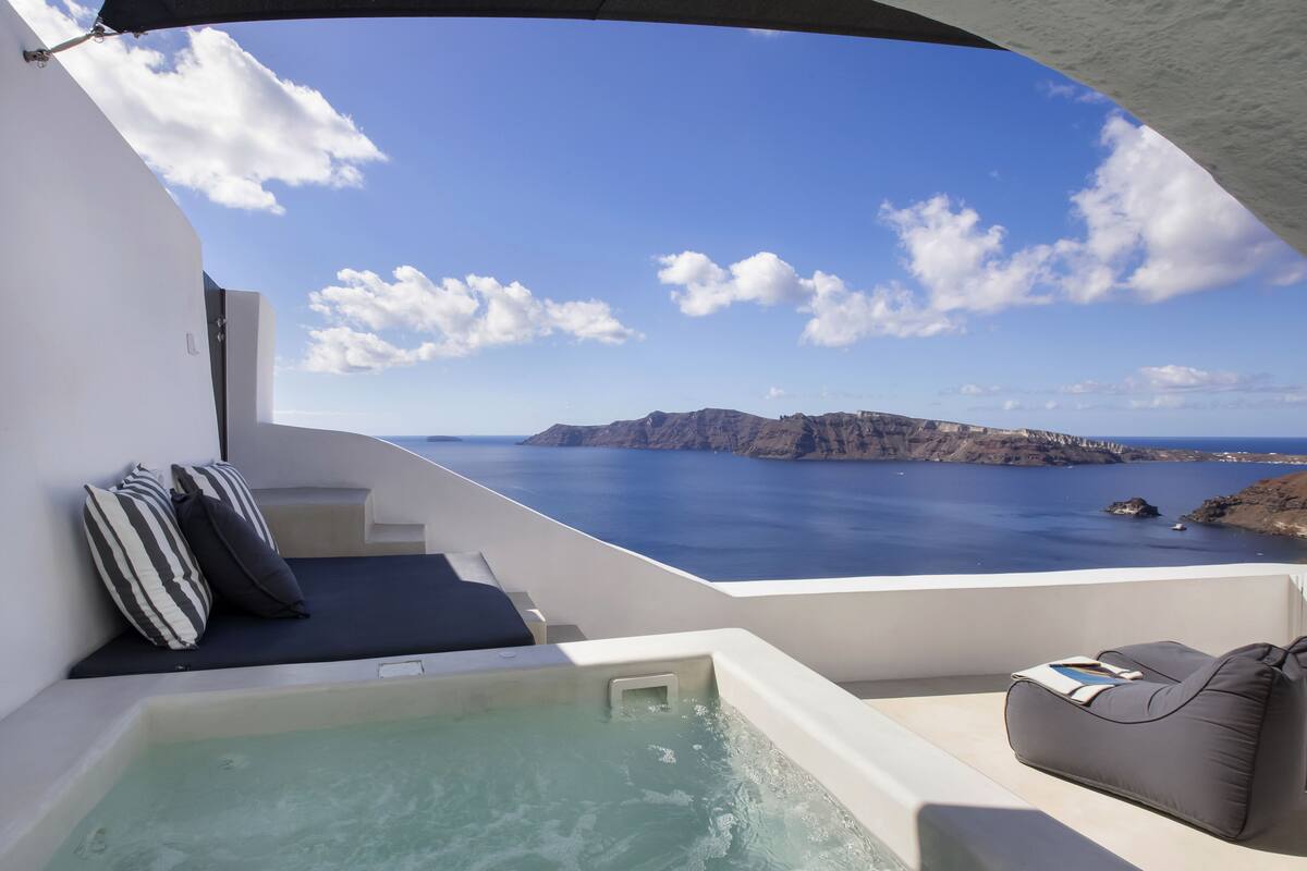 Un balcón con un jacuzzi, cojines y vista al mar y acantilados.