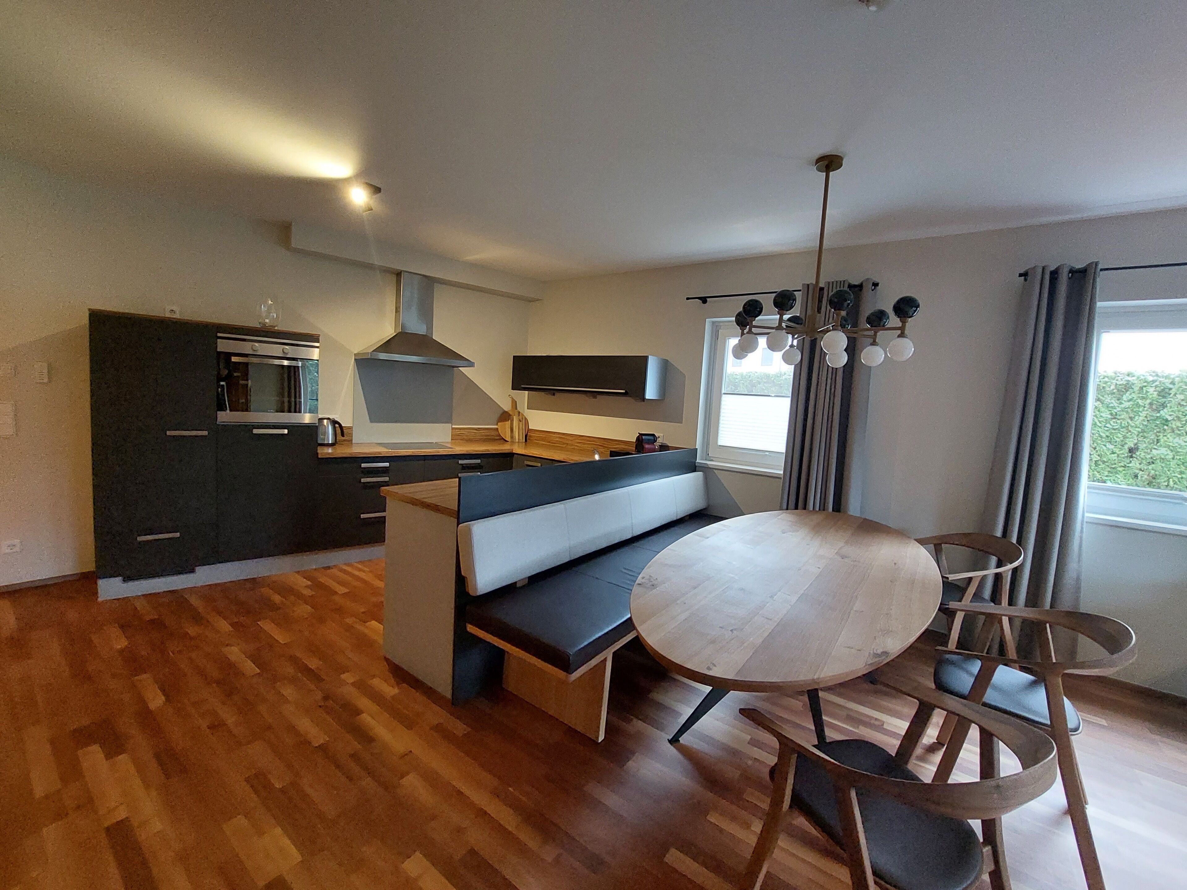 A modern kitchen with dark cabinetry, a built-in oven, and a central island with seating.
