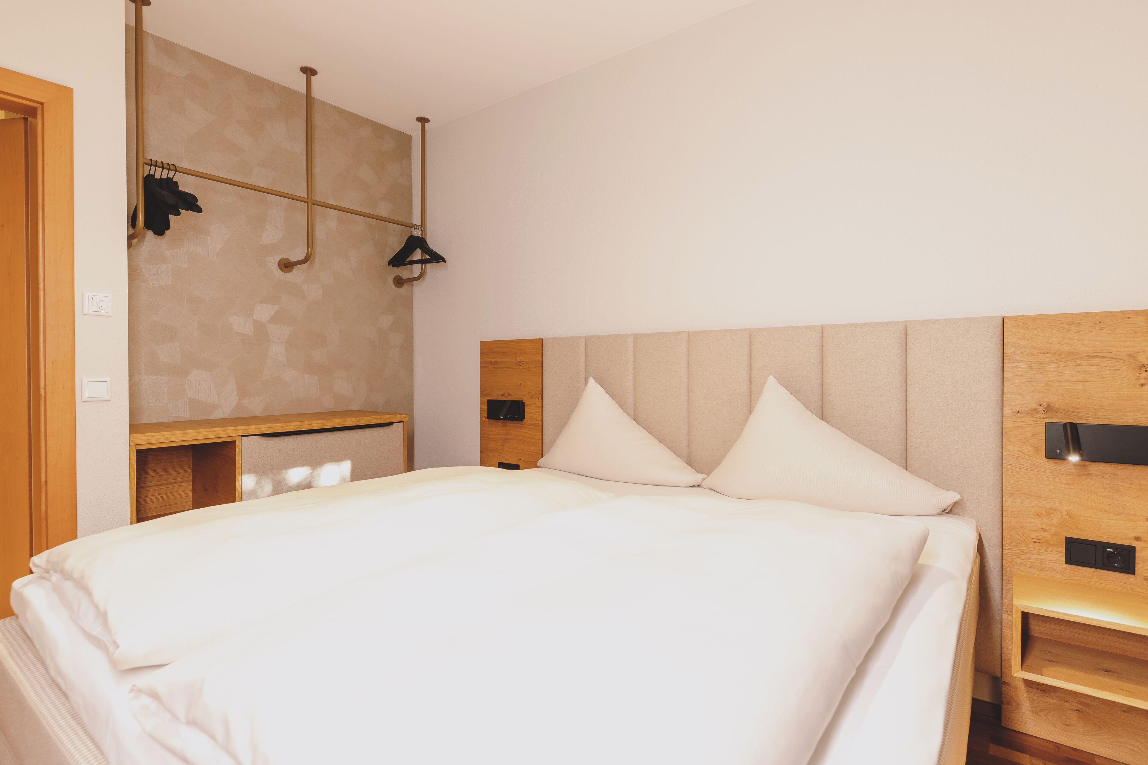 A neatly made bed with a wooden headboard, a small bedside table, and a wall-mounted light fixture.