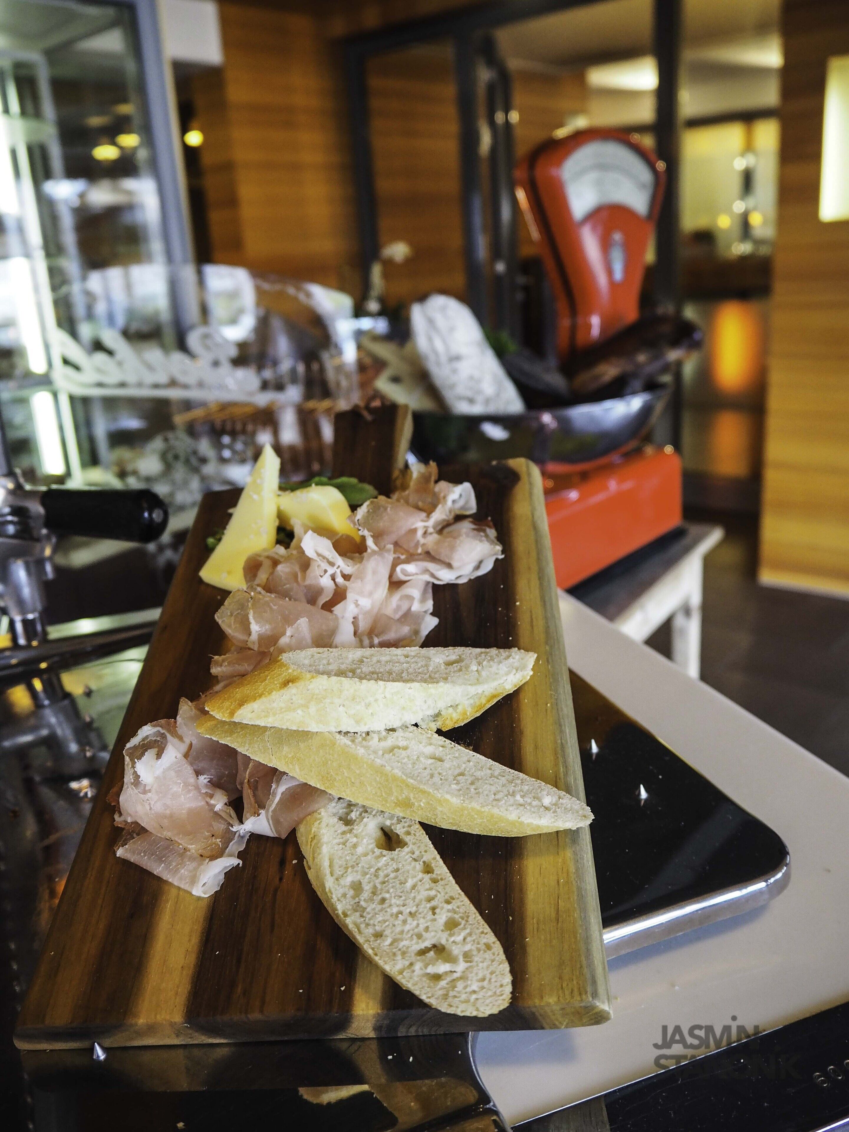 Una tabla de madera con pan en rodajas y embutidos sobre una mesa en un restaurante.