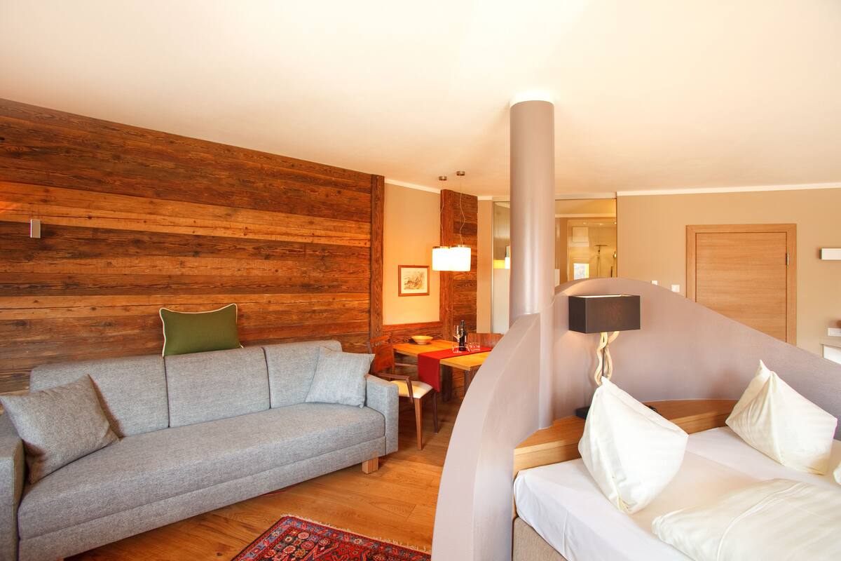Uma sala de estar moderna com uma parede de madeira, um sofá cinzento, um sofá branco, uma mesa de jantar e uma luminária.