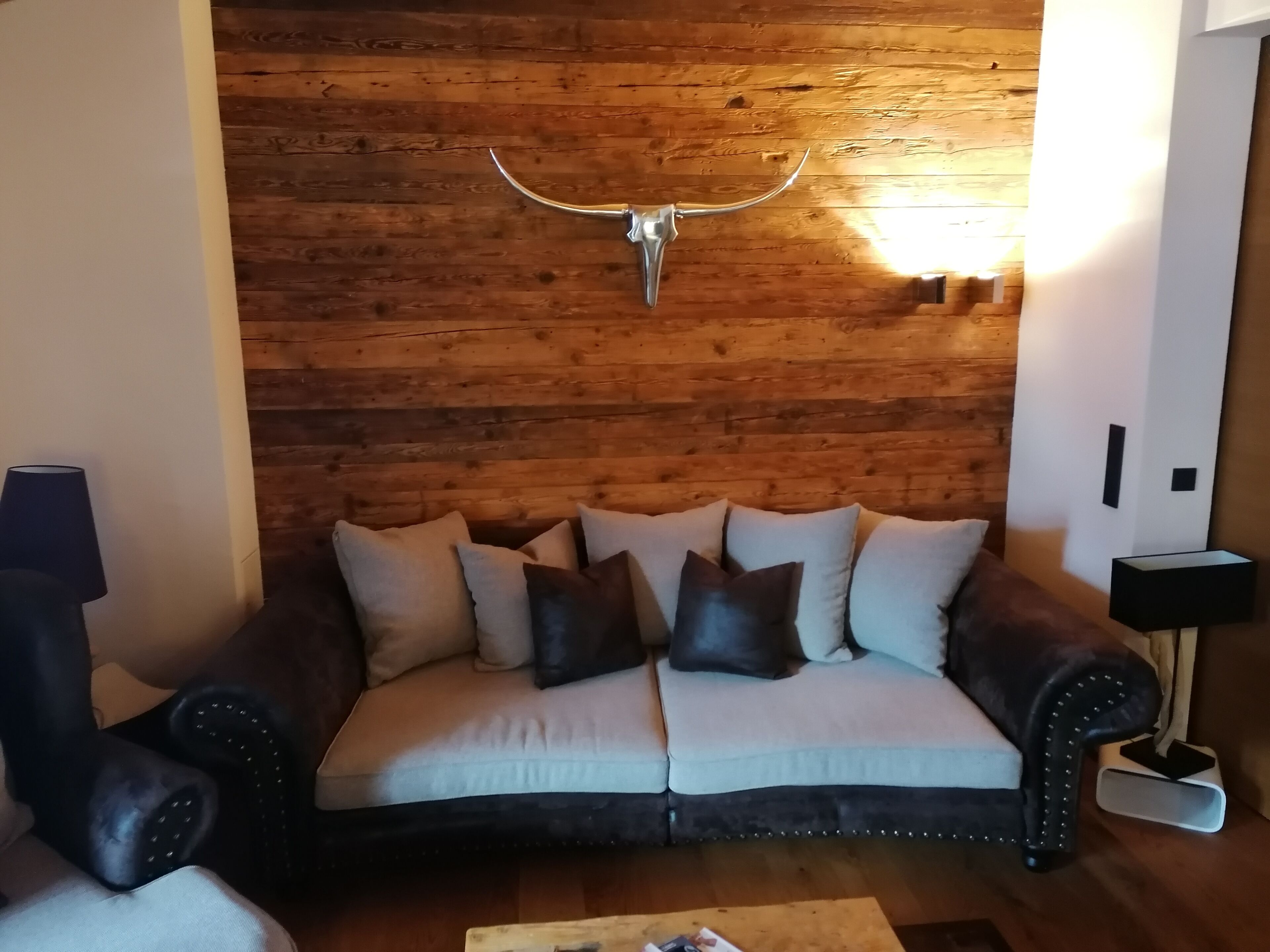A living room with a wooden wall, a sofa with cushions, and a mounted antler.