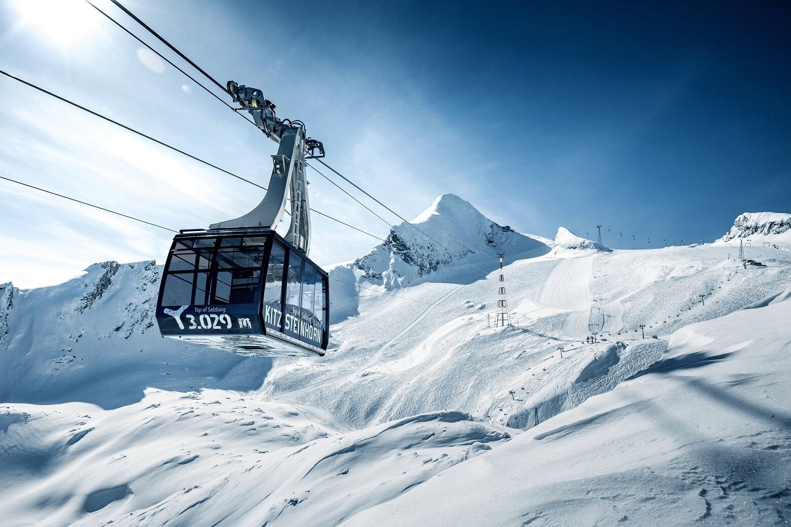 A cable car ascending a snowy mountain with a clear sky.