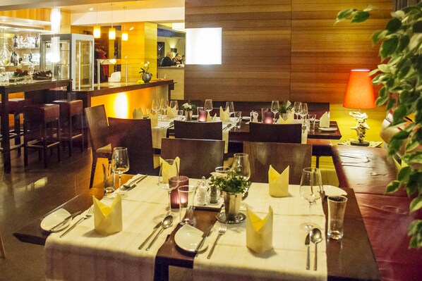 A restaurant with multiple dining tables set for guests, equipped with cutlery, glasses, and candles.