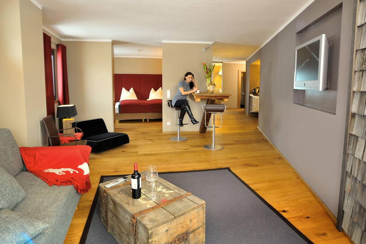 Uma sala de estar moderna com um sofá cinza, uma mesa de centro de madeira, um cobertor vermelho e uma garrafa de vinho.