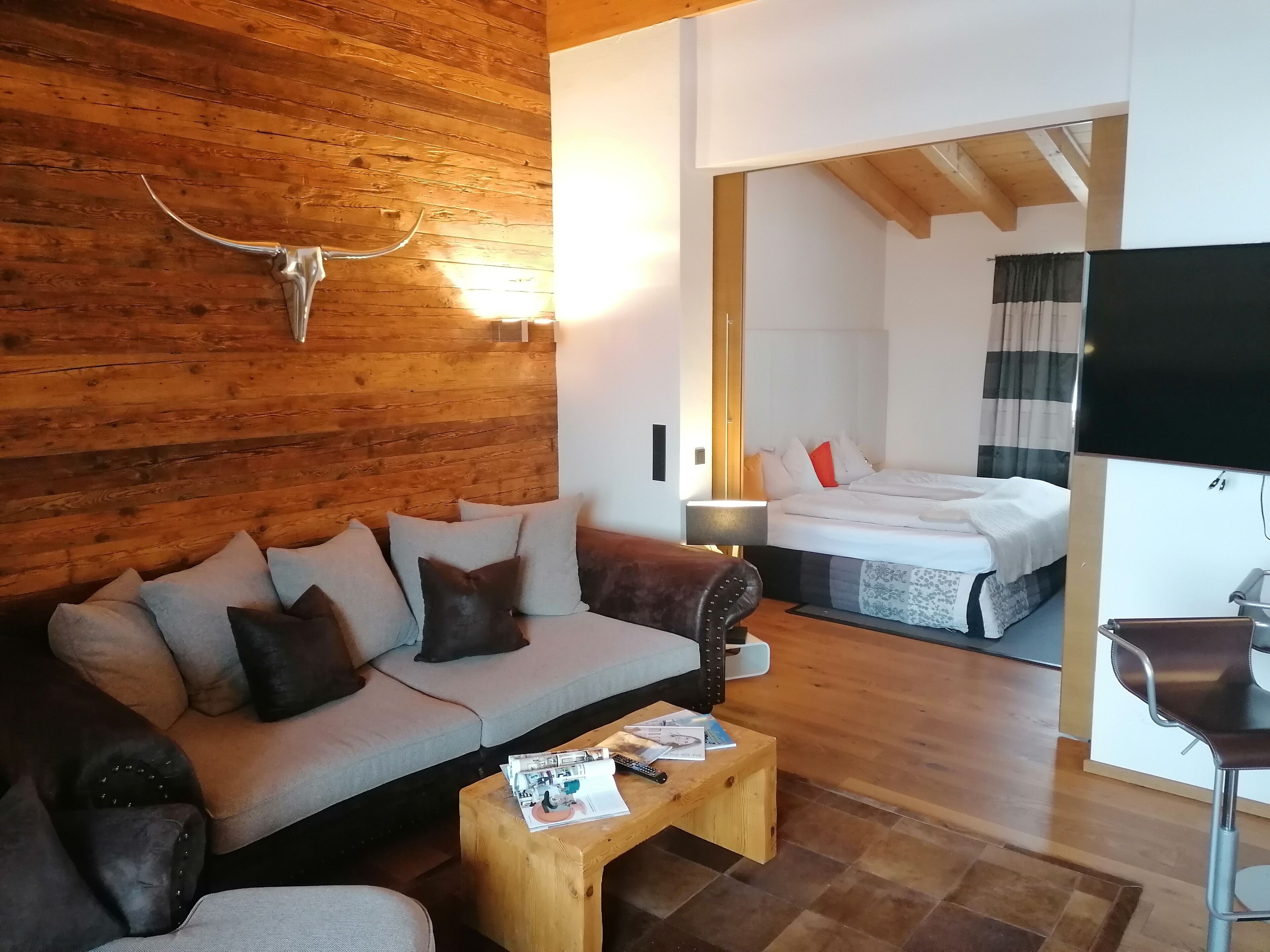 A cozy room with a wooden wall, a sofa with cushions, a small wooden coffee table, and a bed with a white and red bedspread.
