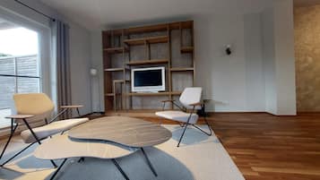 A modern living room with a large TV, wooden shelving, and two chairs.
