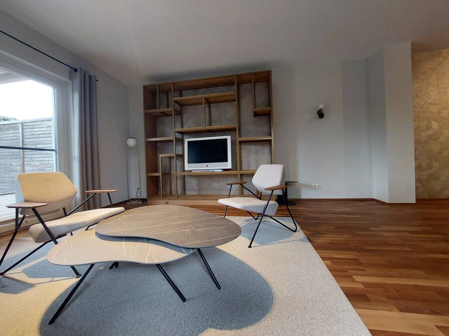 A modern living room with a large TV, wooden shelving, and two chairs.
