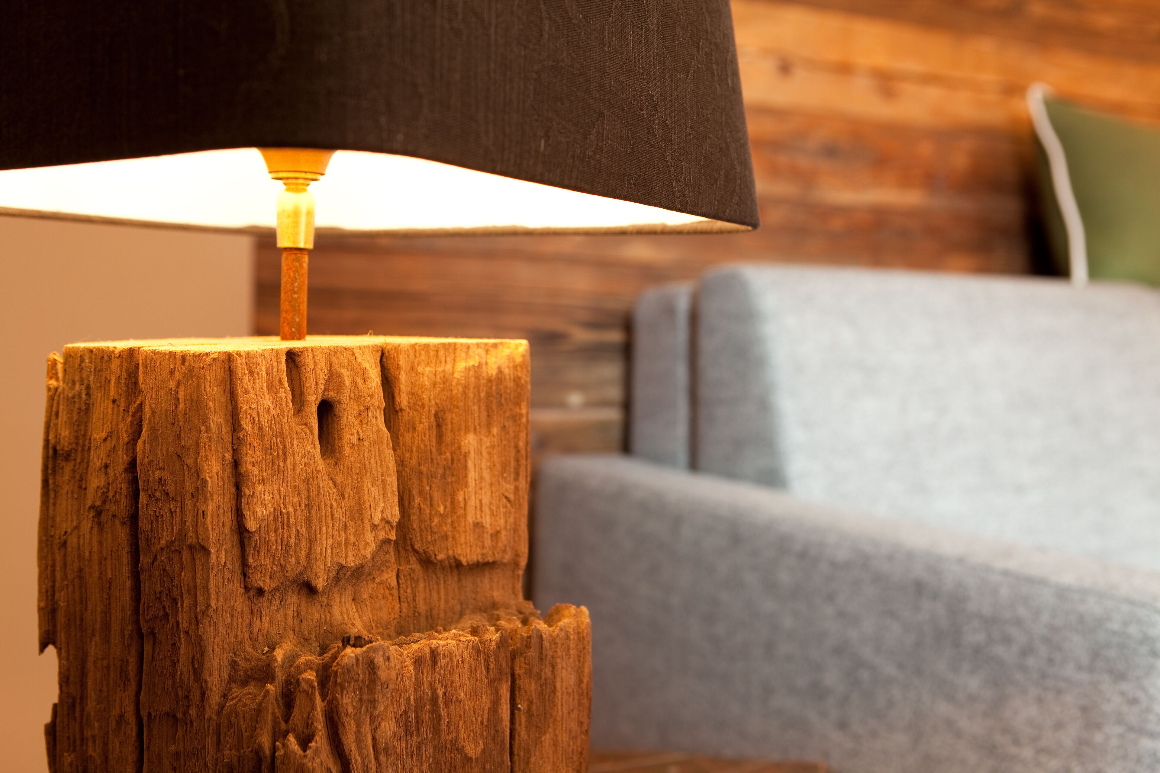 Een houten lantaarnpaal met een zwarte lampenkap in een kamer met een houten wand en een grijze bank.