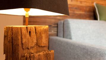 Een houten lantaarnpaal met een zwarte lampenkap in een kamer met een houten wand en een grijze bank.