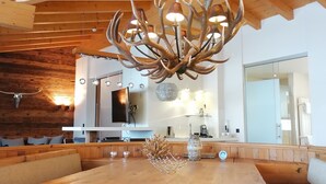 Un espace de restauration moderne avec un plafond en bois, un lustre orné de branches évoquant des bois de cerf, et une grande table en bois avec des sièges.
