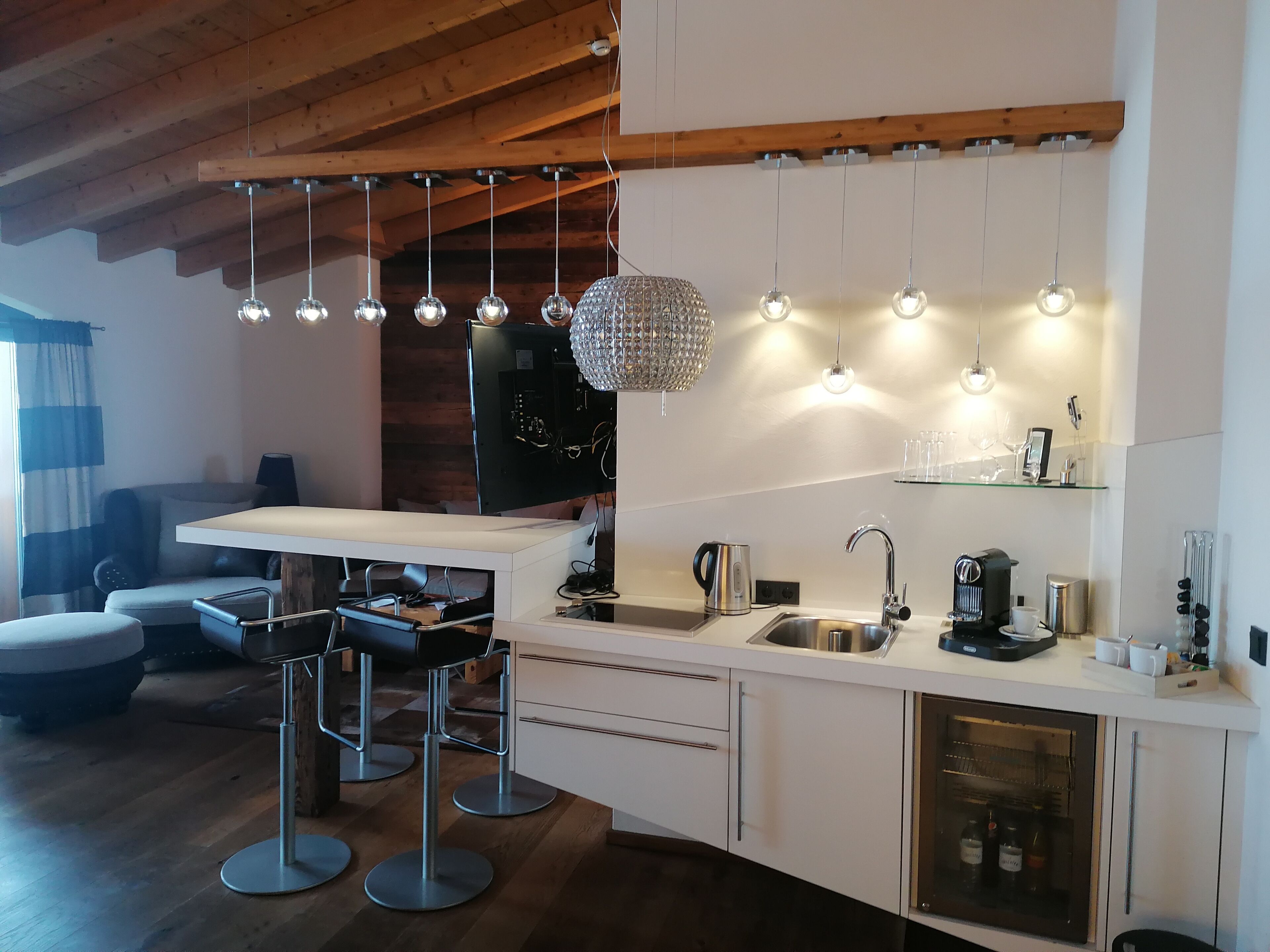 A modern kitchen with a wooden ceiling, pendant lights, a built-in oven, and a bar area with stools.