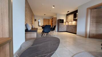 Una sala de estar moderna con un sofá negro curvo, un comedor con una mesa y sillas de madera, y una cocina con horno y microondas integrados.