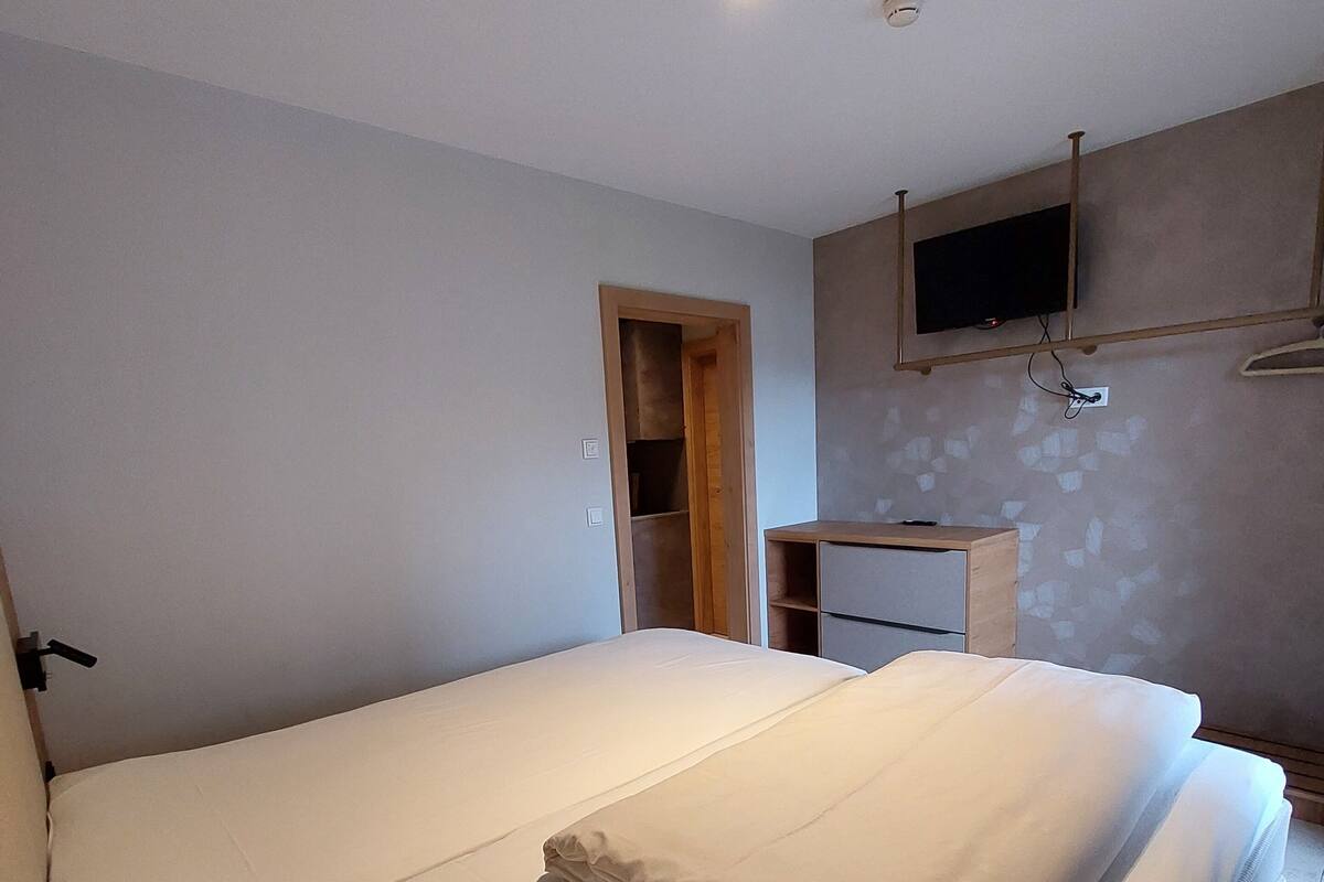 Quarto com uma cama grande, televisão fixada na parede e guarda-roupa de madeira.
