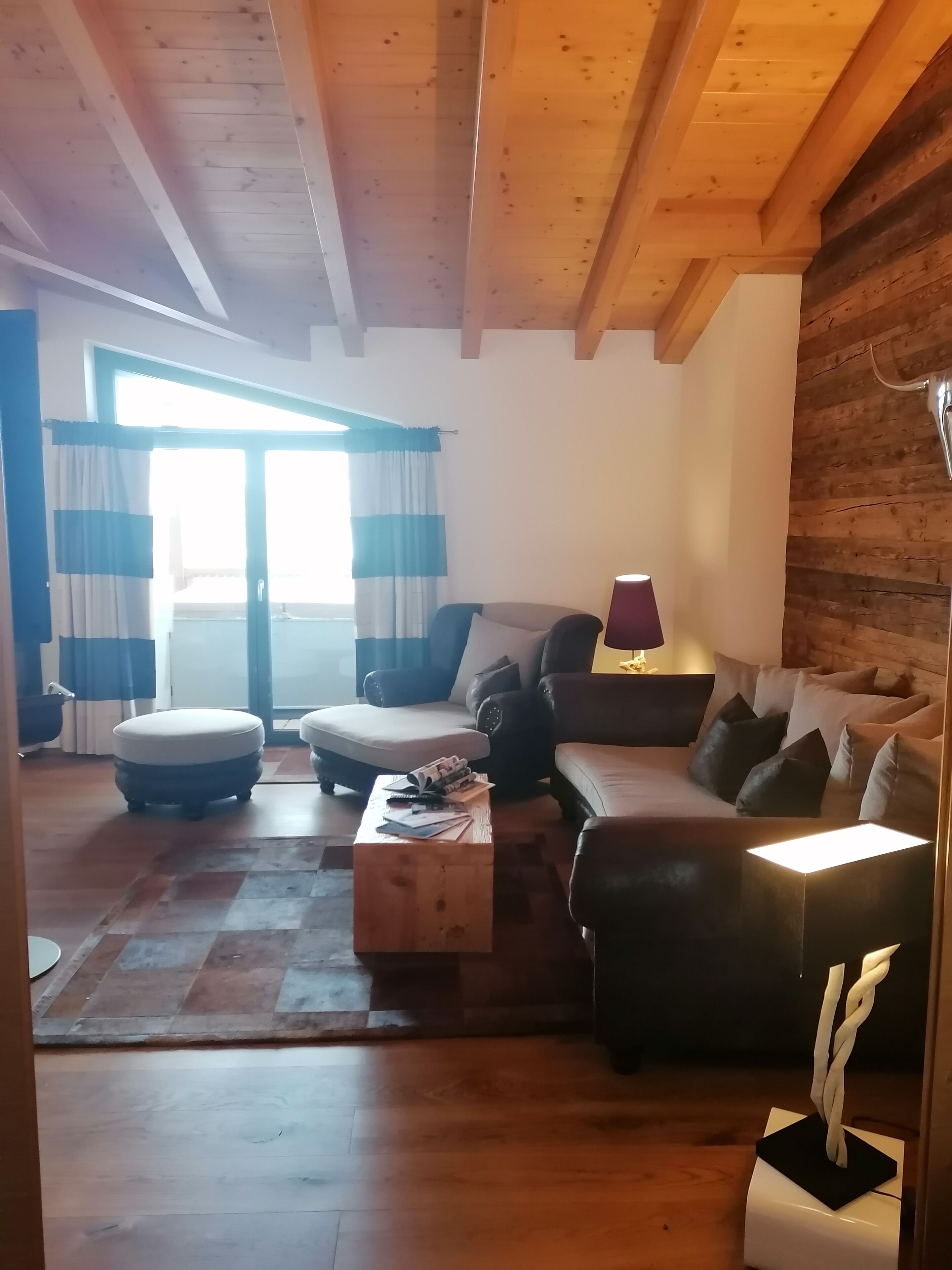 Una sala de estar acogedora con techo de madera, un conjunto de sofá, una mesita de centro con revistas y una lámpara.
