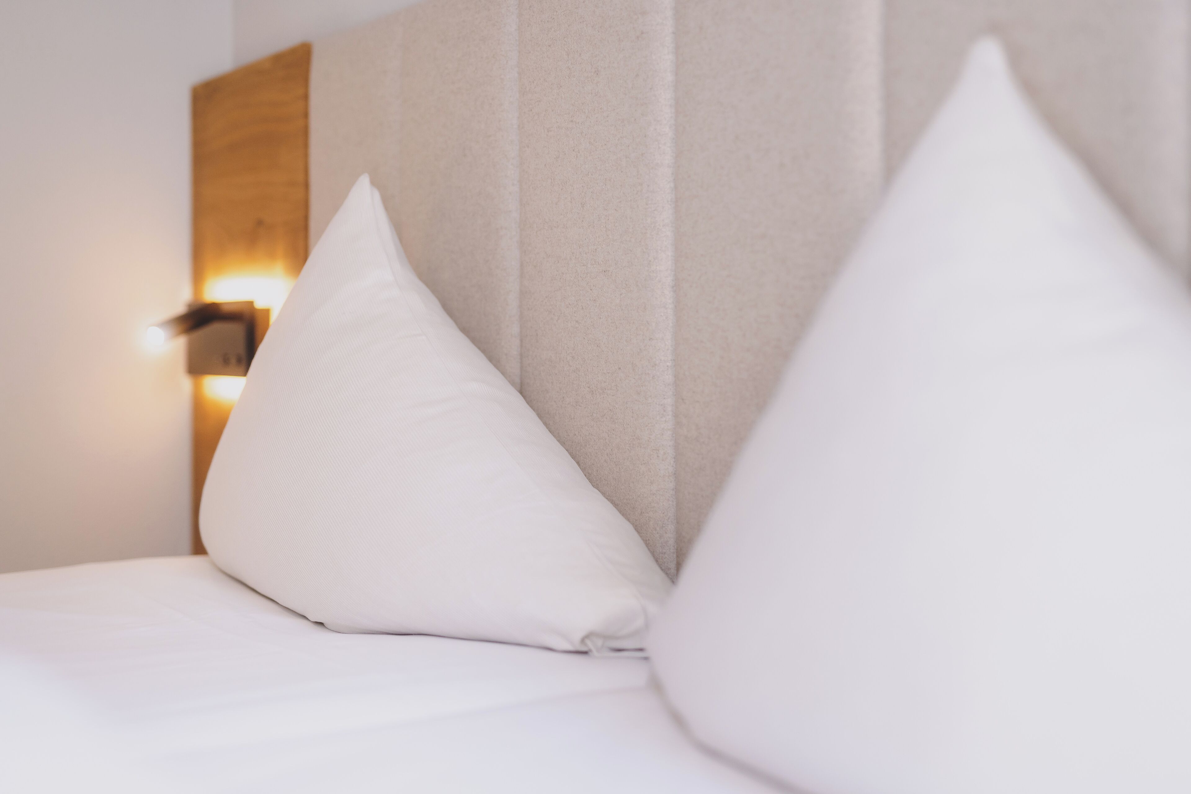 A bed with white pillows and a headboard with a light fixture.