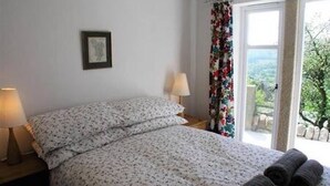 Ein Schlafzimmer mit einem Bett, zwei Nachttischlampen, einem gerahmten Bild an der Wand und einem Fenster mit Blick auf Grünflächen.