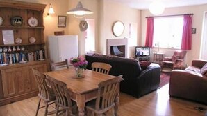 Ein gemütliches Wohnzimmer mit einem Holzesstisch, Stühlen, einer Couch und einem Fernseher.