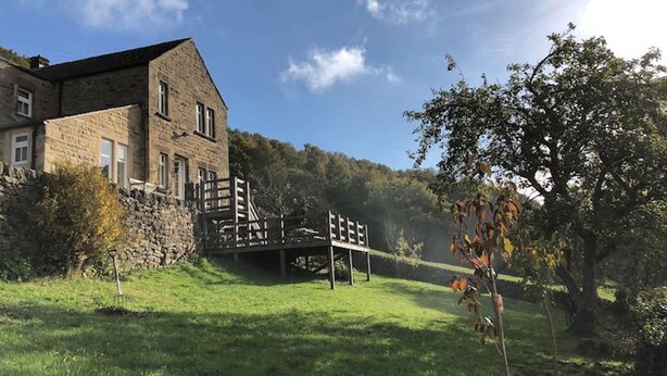 Ein Steinhaus mit einer Holzterrasse und einer Treppe, die zu einer Brücke führt.