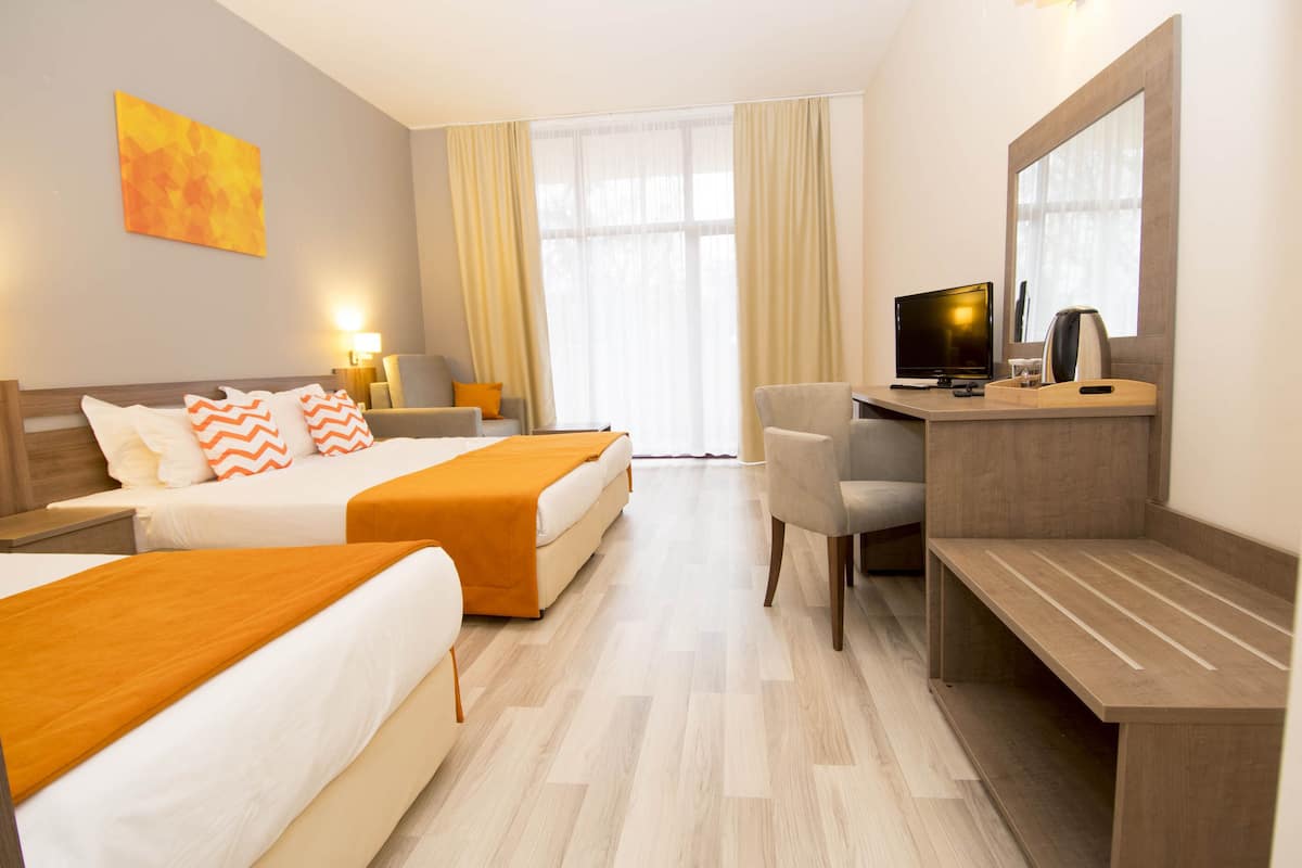 Une chambre d’hôtel avec deux lits, un bureau, une chaise, une télévision et une grande fenêtre avec des rideaux.