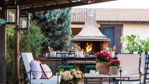 An outdoor patio with a brick fireplace, wicker baskets of fruit, and outdoor seating. - Farmhouse in Maremma a few steps from the sea (Albinia)