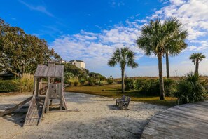 A beach with a wooden lifeguard tower, palm trees, and a sandy area with chairs.
