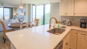 A modern kitchen with a large island, white cabinetry, and a view of the outdoors.