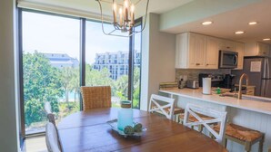 A modern kitchen with white cabinets, a stainless steel refrigerator, and a dining area with a wooden table and wicker chairs.