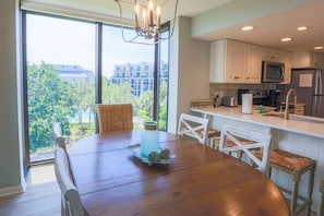 A modern kitchen with white cabinets, a stainless steel refrigerator, and a dining area with a wooden table and wicker chairs.