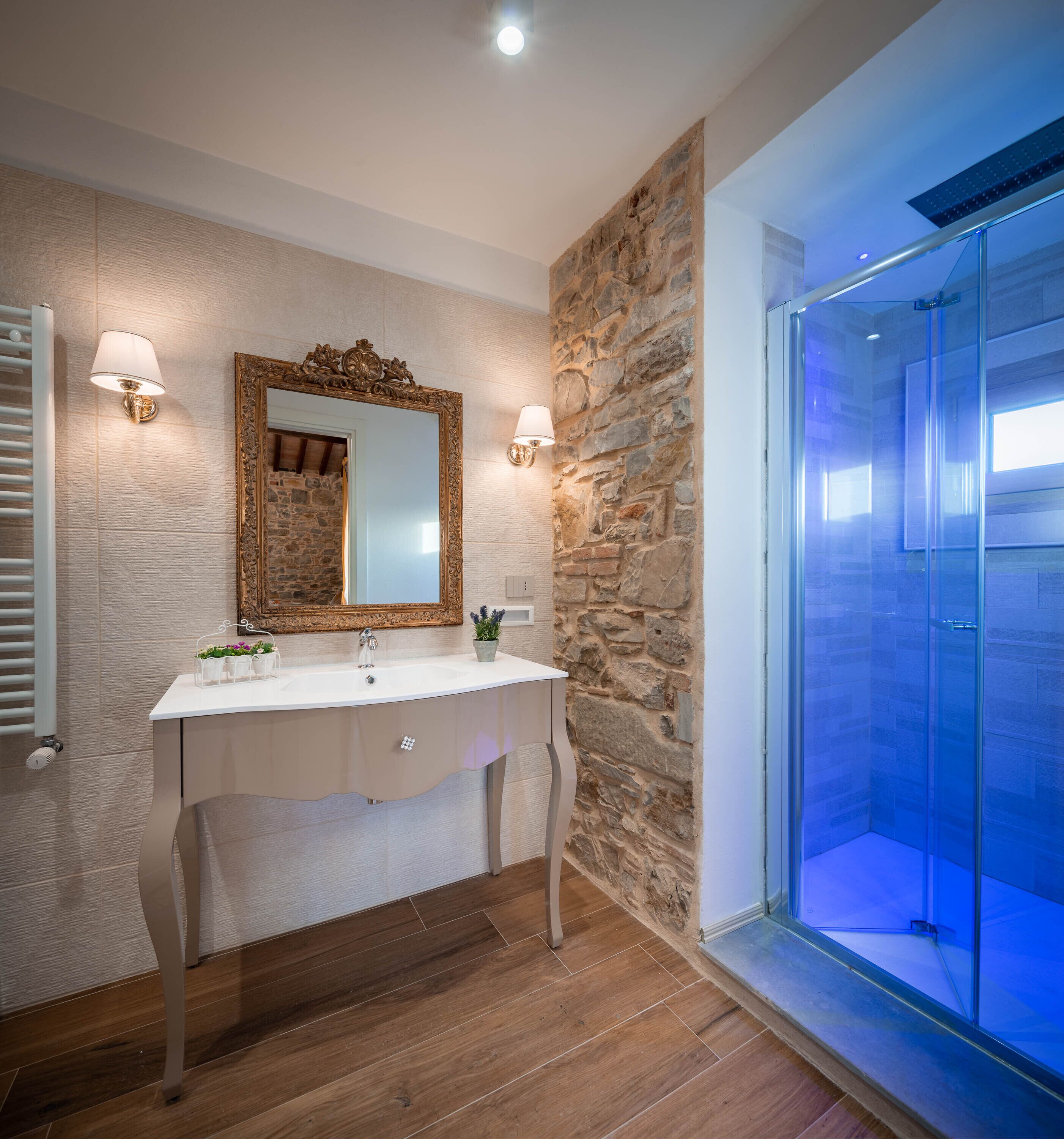 A bathroom with a stone wall, a white sink with a mirror, and a glass shower enclosure.