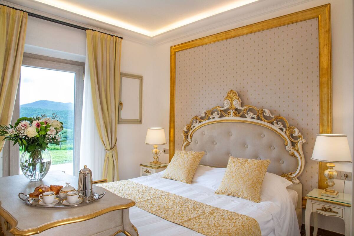 A hotel room with a large bed, two bedside tables with lamps, a window with curtains, and a view of the outdoors.