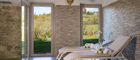 Un cuarto de spa con dos camastros, una pared de piedra y vistas a un jardín.