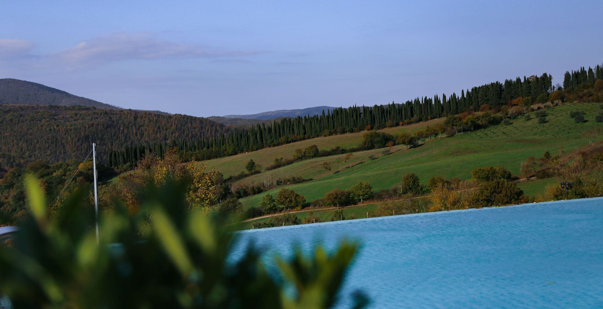 A pool with a view of a hilly landscape and trees.