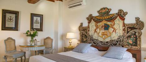 A bedroom with a large bed, two chairs, a small table, and ornate headboard.