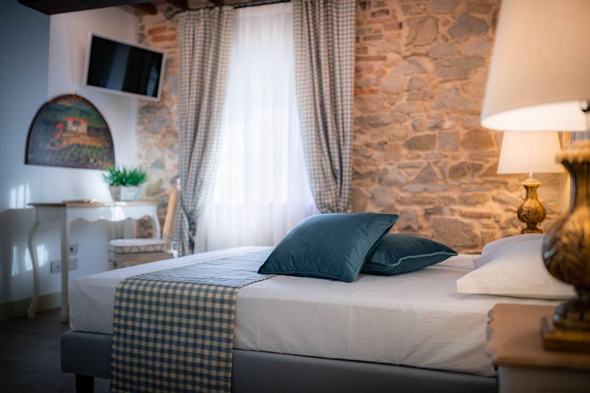 A neatly arranged bedroom with a bed, a bedside table, a lamp, and a stone wall.