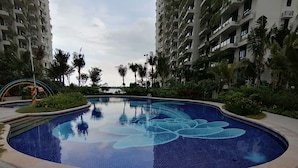 A swimming pool with a floral design, surrounded by palm trees and high-rise buildings. - Forest City Ataraxia Park 4  by Wastone (Gelang Patah)