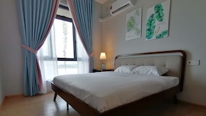 A neatly made bed in a room with a wooden floor, a window with blue curtains, and wall art depicting leaves. - Forest City Ataraxia Park 4  by Wastone (Gelang Patah)