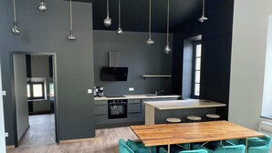 A modern kitchen with a central island, a dining area with teal chairs, and pendant lighting. - Le Loft de la Tour Pinte (Carcassonne)