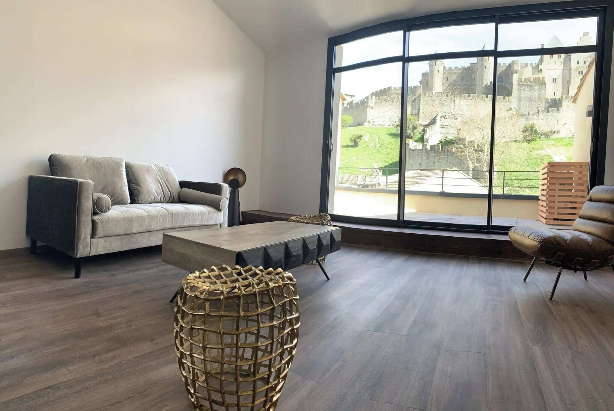 Un salon moderne avec une grande fenêtre, un canapé, une table basse et une petite table d’appoint en osier.