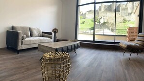 A modern living room with a large window, a sofa, a coffee table, and a wicker side table. - Le Loft de la Tour Pinte (Carcassonne)