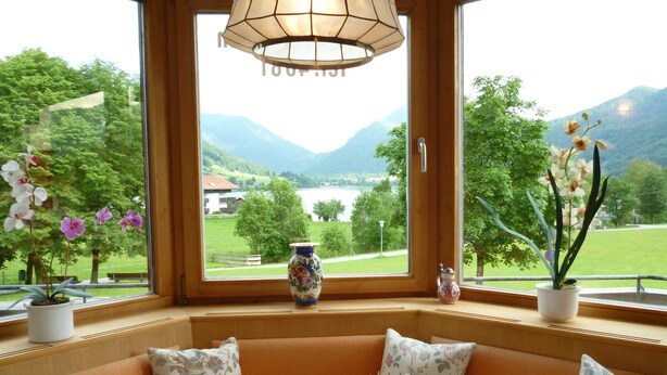 Une pièce avec vue sur les montagnes et un lac, une table ornée d’un vase de fleurs et un banc agrémenté de coussins à motifs floraux.