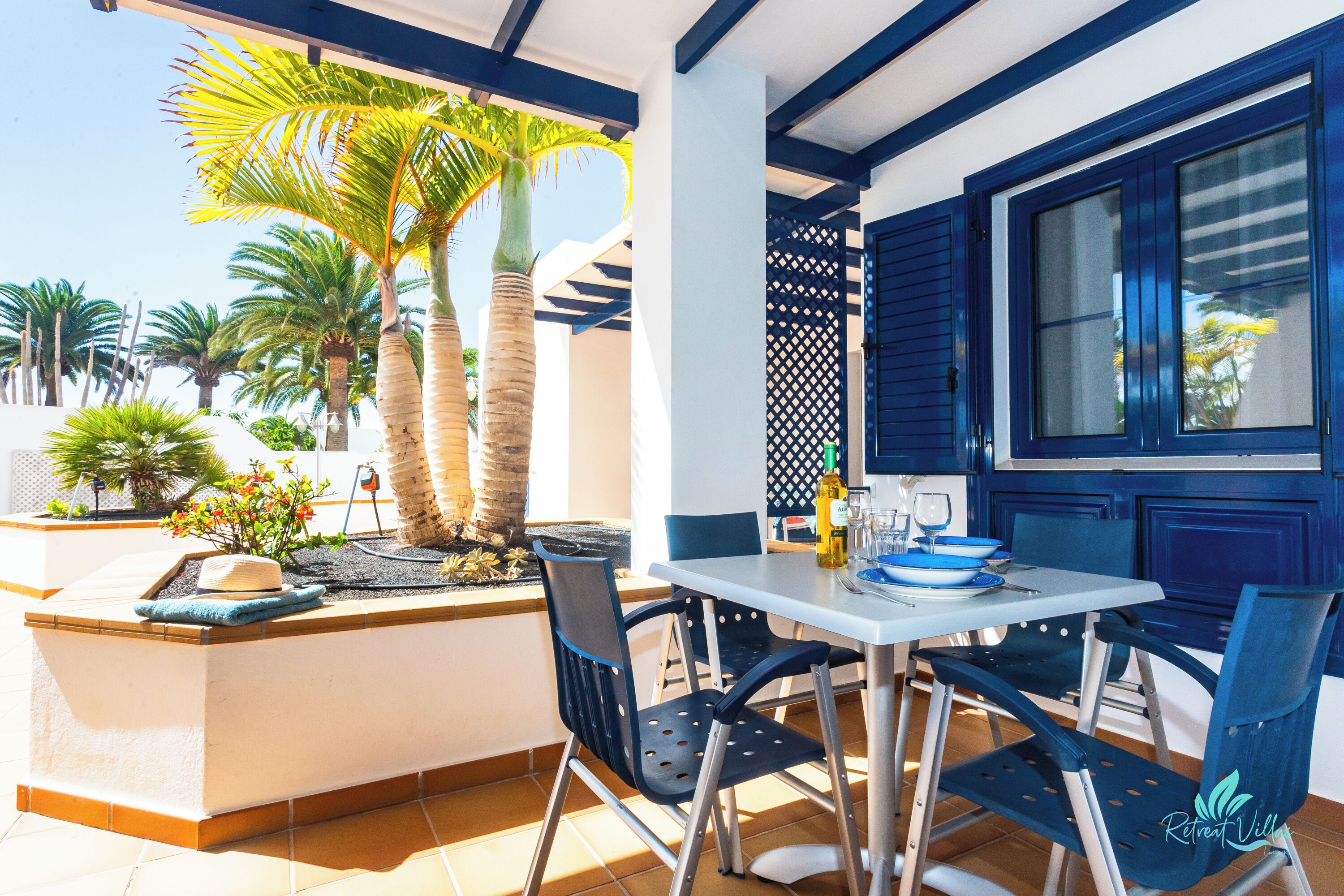 Un patio con mesa y sillas, palmeras y vistas al mar.