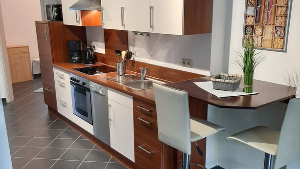 Una cocina moderna con una isla central, electrodomésticos de acero inoxidable y un comedor con taburetes de bar.