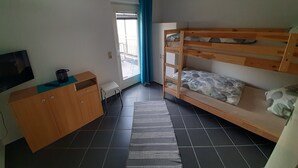 Una habitación con literas, un escritorio pequeño, televisión y una ventana con cortinas.