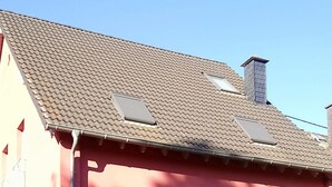 Un edificio de dos plantas con fachada roja, ventanas grandes y techo de tejas.