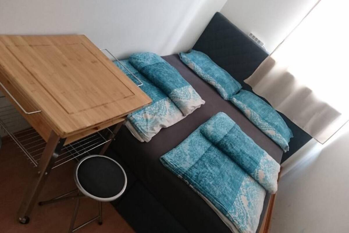 A small room with a bed, a wooden table, and a small stool.